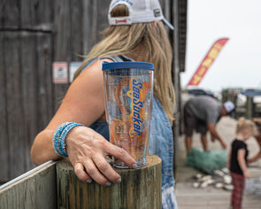 This cup fits in the hand like an old friend. The photo shows a side-view shot of the item, highlighting the vibrant colors of the orange octopus splashing in a bright blue wave, all on the clear plastic material from which the cup is made. Topping it off, literally, is a navy-blue lid that snugly secures the liquid in the vessel.